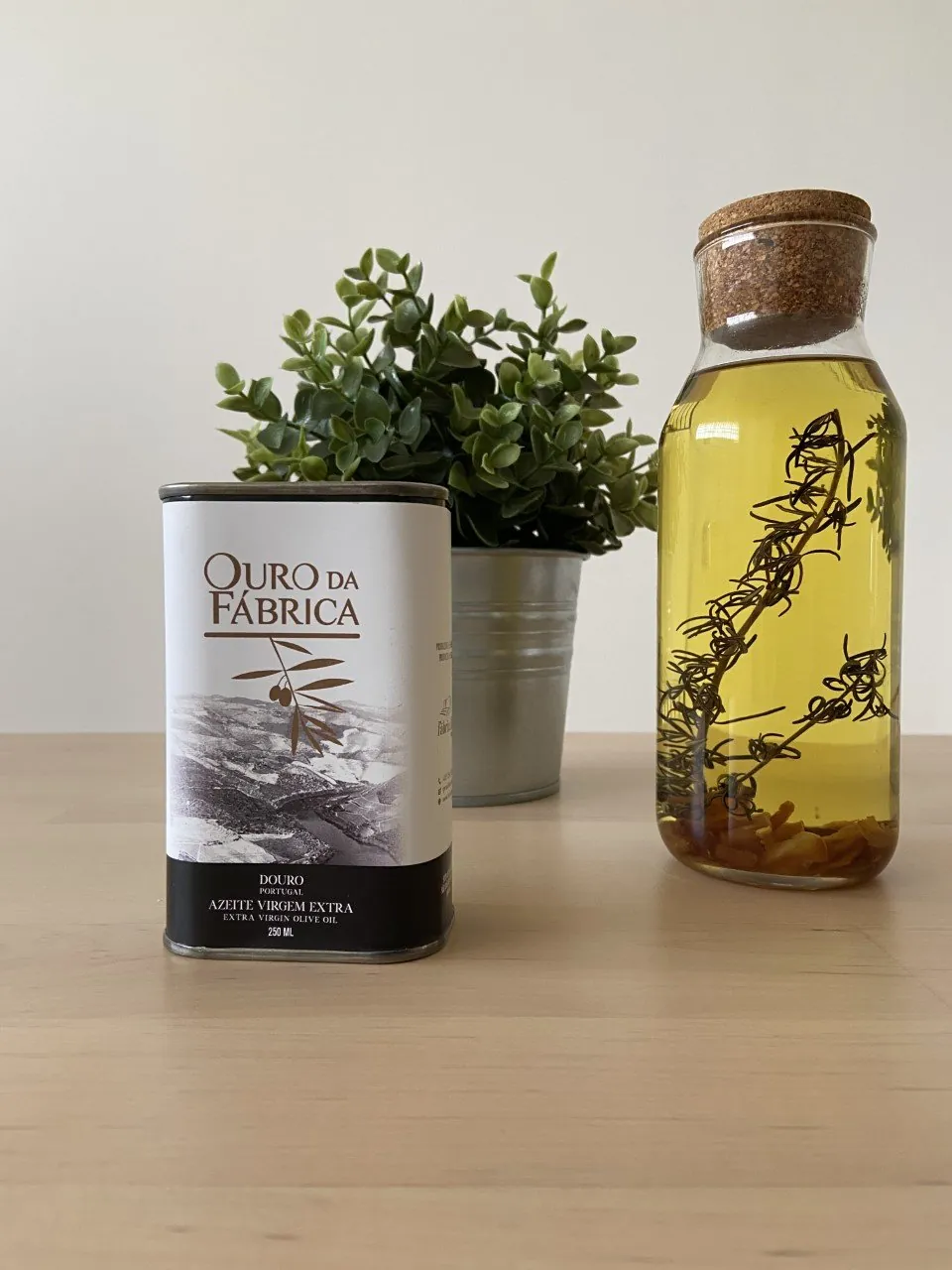 Lata de azeite Ouro da Fábrica ao lado de uma garrafa com ervas